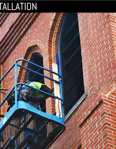 Worker installing new, custom louvered shutters at church bell tower.